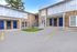 Charming brick apartment complex featuring elegant blue doors, ample parking, and a touch of greenery under a clear blue sky.