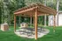 Charming backyard setup with a wooden pergola, picnic tables, and built-in stone grills surrounded by lush greenery.