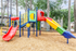 Vibrant playground with colorful slides and climbing structures surrounded by lush greenery, perfect for family-friendly living.