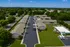 Aerial view of a charming apartment complex with landscaped green spaces, a central parking area, and inviting outdoor amenities under a clear blue sky.