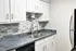 Modern kitchen with sleek granite countertops, stylish white cabinetry, and contemporary brick backsplash.