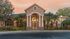 Elegant apartment complex entrance with grand columns, lush landscaping, and warm sunset glow.