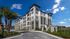 Modern multi-story apartment complex with sleek design, surrounded by lush landscaping and palm trees, under a clear blue sky.