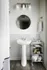 Elegant bathroom featuring a sleek pedestal sink, modern lighting, round mirror, and stylish tile accents.
