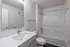 Sleek and modern bathroom featuring a spacious white vanity with a polished faucet, large mirror, and pristine bathtub with shower.