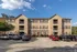 Charming three-story apartment building with modern architectural design, featuring multiple balconies and ample parking under a clear blue sky.