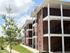 Charming red-brick apartment complex with spacious balconies and lush green surroundings under a bright blue sky.