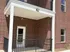 Charming brick apartment exterior featuring a cozy, covered patio with stylish black railing.