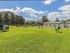 Expansive apartment community park with vibrant green lawn, play equipment, and seating under a clear blue sky.