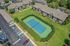 Aerial view of a charming apartment community with landscaped greenery, featuring a well-maintained tennis court and convenient parking facilities.
