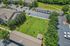 Aerial view of a vibrant apartment community featuring lush green lawns, a fenced dog park, and convenient parking spaces surrounded by charming buildings.