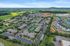 Aerial view of a vibrant apartment complex surrounded by lush greenery, featuring modern buildings, ample parking, and a central tennis court.