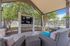 Inviting outdoor lounge area with comfortable wicker seating, a large TV, and lush greenery, perfect for relaxation and entertainment.