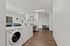 Bright and modern laundry room with wood flooring, featuring multiple washers and a cozy seating area, ideal for a convenient apartment living experience.