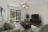 Bright and inviting living room with modern decor, featuring a plush green sofa, stylish coffee table, sleek TV unit, and large window with garden view.