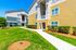 Sunlit apartment complex with bright yellow and gray exterior, surrounded by lush greenery and well-maintained pathways.
