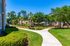 Charming apartment exterior with lush greenery, palm trees, and sunny pathways in a vibrant community setting.