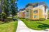 Charming apartment complex with vibrant siding, lush landscaping, and a winding pathway under a clear blue sky.