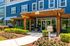 Charming apartment complex entrance with lush landscaping, inviting wooden pergola, and modern glass doors.