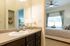 Inviting bedroom with plush bedding, cozy decor, and a modern en-suite bathroom featuring elegant vanity lighting.