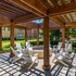 Inviting outdoor patio with a wooden pergola and cozy fire pit surrounded by white Adirondack chairs, perfect for relaxation.