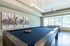 Elegant recreational space featuring a modern pool table, vibrant abstract artwork, and large windows offering natural light.