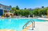 Inviting outdoor pool area with sun loungers and shaded seating, surrounded by lush palm trees and modern apartments.