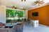 Charming outdoor living space featuring cozy wicker seating, bar area with granite countertop, ceiling fans, and a lush garden view.