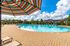 Inviting outdoor pool area with colorful sun umbrellas and luxurious loungers, framed by vibrant greenery and a clear blue sky.
