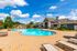 Luxurious apartment complex featuring a sparkling pool surrounded by elegant lounge chairs and lush greenery under a clear blue sky.