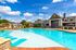 Luxurious apartment complex featuring a sparkling blue swimming pool, surrounded by lush landscaping and elegant lounge chairs under a bright, sunny sky.