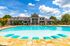 Luxurious apartment complex featuring a stunning outdoor pool with turquoise lounge chairs, surrounded by lush greenery and an inviting clubhouse under a vibrant blue sky.