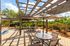 Charming outdoor patio with stylish pergola, vibrant striped umbrellas, and comfortable seating surrounded by lush greenery.