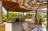 Charming outdoor patio area featuring colorful umbrellas, a stone barbecue grill, and lush greenery, perfect for entertaining and relaxation.
