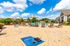 Vibrant outdoor area with a refreshing swimming pool, luxurious lounge chairs, and a fun cornhole setup under a bright blue sky, perfect for relaxation and entertainment.