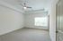Bright and spacious bedroom with soft carpet, large window, and modern ceiling fan, offering a serene retreat.