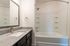 Modern bathroom with sleek granite countertops, elegant mirror, and a pristine white bathtub with a shower.