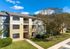 Charming apartment complex with spacious balconies, surrounded by lush greenery and vibrant trees under a clear blue sky.