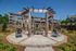 Charming outdoor space featuring a rustic wooden pergola with a stone fire pit, lush landscaping, and stylish seating, ideal for relaxation and social gatherings.