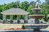 Elegant outdoor scene of a charming stone fountain with cascading water, set against a backdrop of a landscaped garden and pavilion, perfect for relaxation and events.