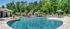 Luxurious outdoor pool area surrounded by lush greenery, featuring elegant cabanas and a relaxing patio with umbrellas.