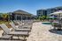 Elegant outdoor pool area with sun loungers, umbrellas, and modern apartment buildings in a landscaped setting.