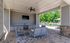 Inviting covered patio with cozy seating, flat-screen TV, and outdoor kitchen, overlooking a lush pool area with vibrant greenery.