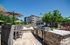 Luxurious outdoor living space with a modern stone grill station, patio seating, and umbrella-shaded lounging area against a backdrop of a stylish apartment complex.