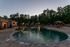 Elegant outdoor pool area surrounded by lush greenery at twilight, featuring cozy cabanas and stylish patio seating.