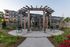 Beautiful outdoor space featuring a wooden pergola, cozy seating, and a stone fire pit surrounded by lush greenery in a modern apartment community.