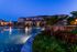 Luxury apartment complex at dusk with a serene pool, illuminated reflections, and lush landscaping.