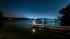 Serene nighttime lake view featuring a tranquil dock, shimmering water, and distant illuminated shoreline.