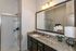 Elegant bathroom with granite countertop, spacious mirror, and modern shower, accented by a stylish lamp and orchid plant.