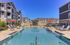 Luxurious apartment complex featuring a sparkling pool, elegant sun loungers, and stylish apartment buildings with balconies basking in a bright blue sky.